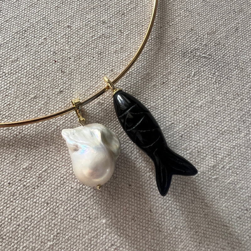 Gold necklace with a black fish-shaped pendant and a white pearl on a gray fabric background