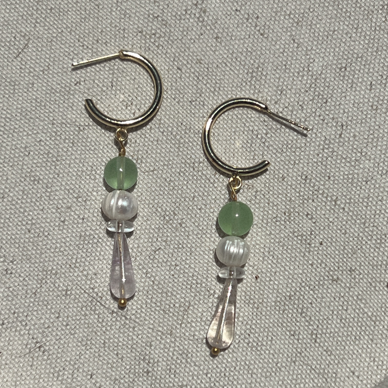 Pair of earrings with green and clear beads on a textured gray background
