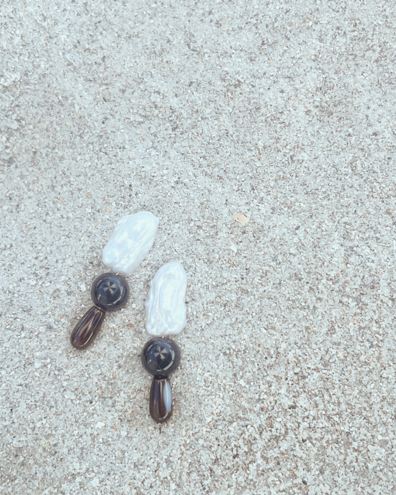 Two earrings with white stones and brown accents on a light gray surface