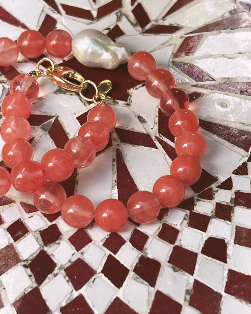 Red beaded bracelet with a gold clasp on a mosaic background