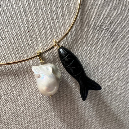 Gold necklace with a black fish-shaped pendant and a white pearl on a gray fabric background