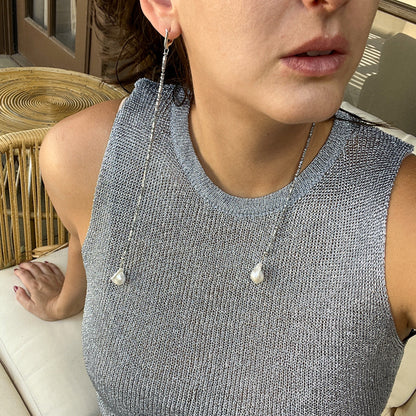 A close-up lifestyle shot of a woman wearing a silver beaded chain necklace with two large white baroque pearl drops, paired with a textured gray sleeveless top.
