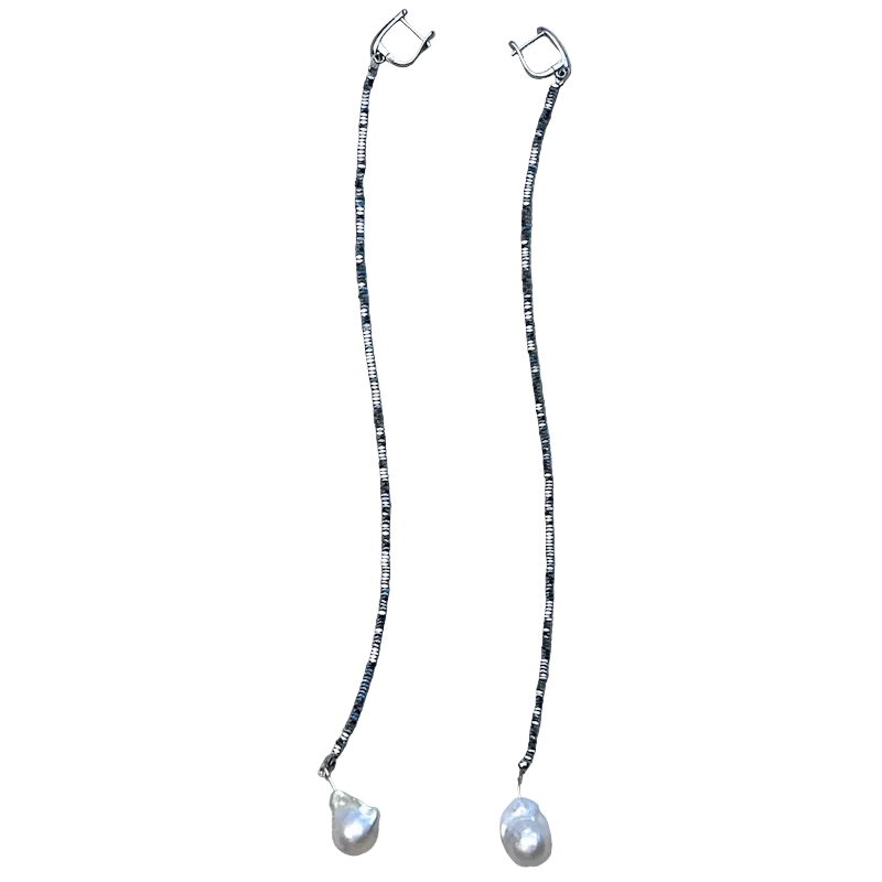 A pair of long drop earrings with silver-toned hoops connected by thin beaded chains, each ending in a teardrop-shaped white pearl, displayed on a textured beige fabric background.