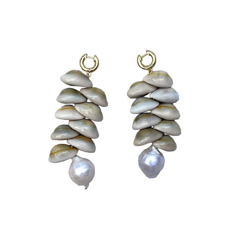 A pair of handmade dangle earrings featuring stacked natural clam shells in beige and gray tones, with a small gold hoop at the top and a single baroque pearl dangling at the bottom, displayed on a textured beige linen background.