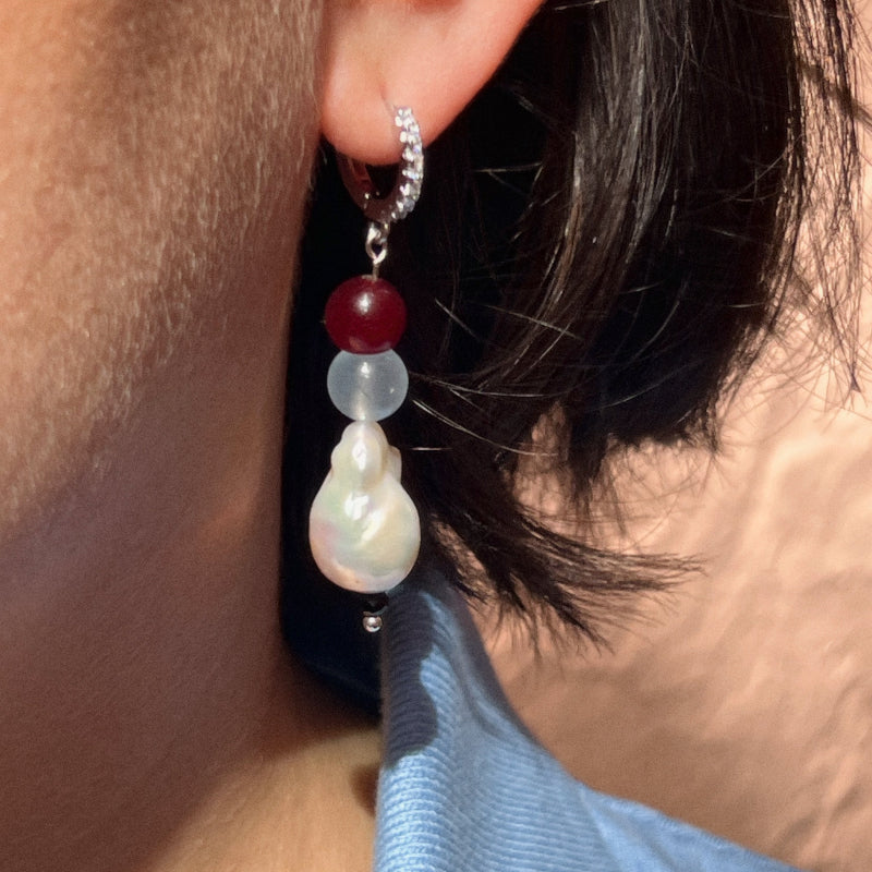 Close-up of an earring with beads worn by a person against a neutral background