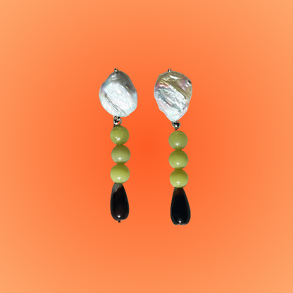 Pair of earrings with green beads and black accents on an orange background