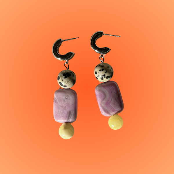Pair of earrings with purple and gold beads on an orange background