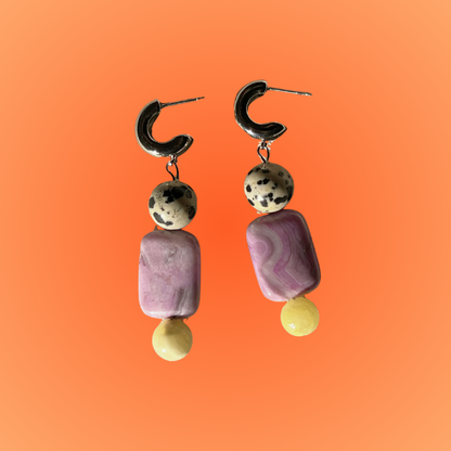 Pair of earrings with purple and gold beads on an orange background