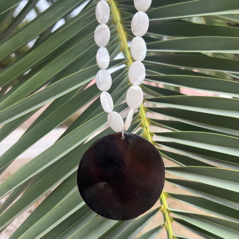 Necklace with white beads and a dark brown pendant on a palm leaf background