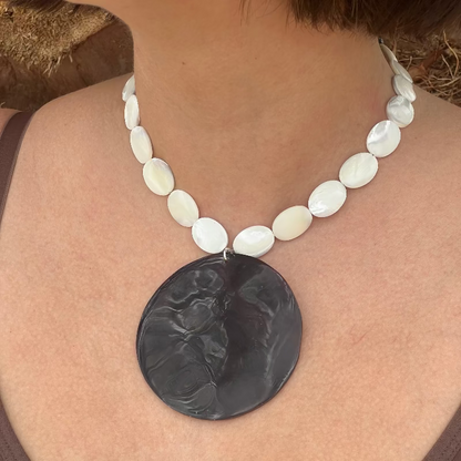 Necklace with a large black pendant and white beads on a person wearing a brown top.