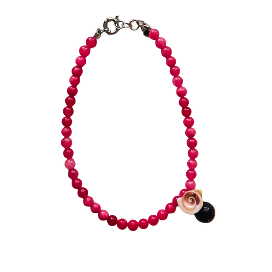 Pink beaded bracelet with a black and gold charm on an orange gradient background