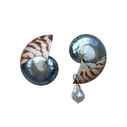 A pair of earrings made from spiral nautilus shells with iridescent blue-gray and brown patterns, each hanging from a small white pearl drop, displayed on a textured beige fabric background.