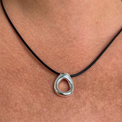 Close up of simple circular leather necklace with a small organically shaped circular sterling silver pendant.